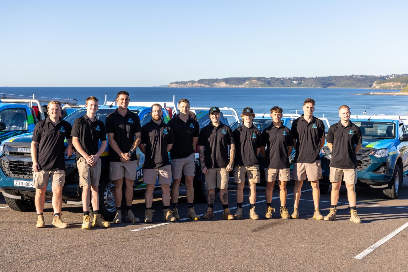 The Rae.co Plumbing team lined up with their trucks at the beach